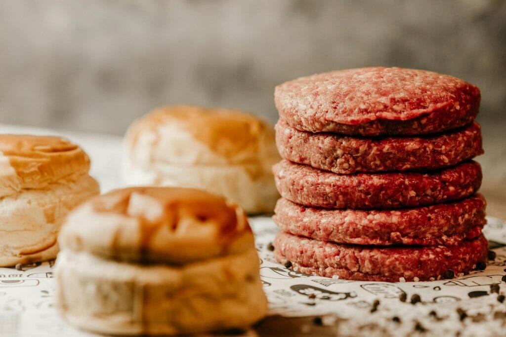 A stack of fresh raw beef patties with nearby burger buns, ready for cooking.