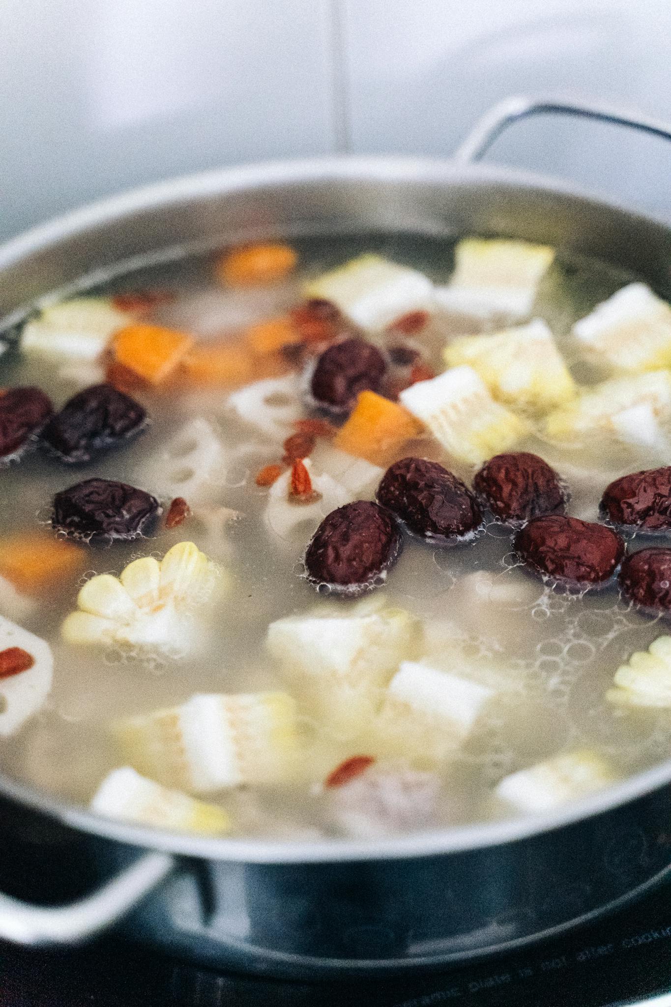 Close-up of a simmering vegetable soup with corn, carrots, dates, and herbs in a pot.